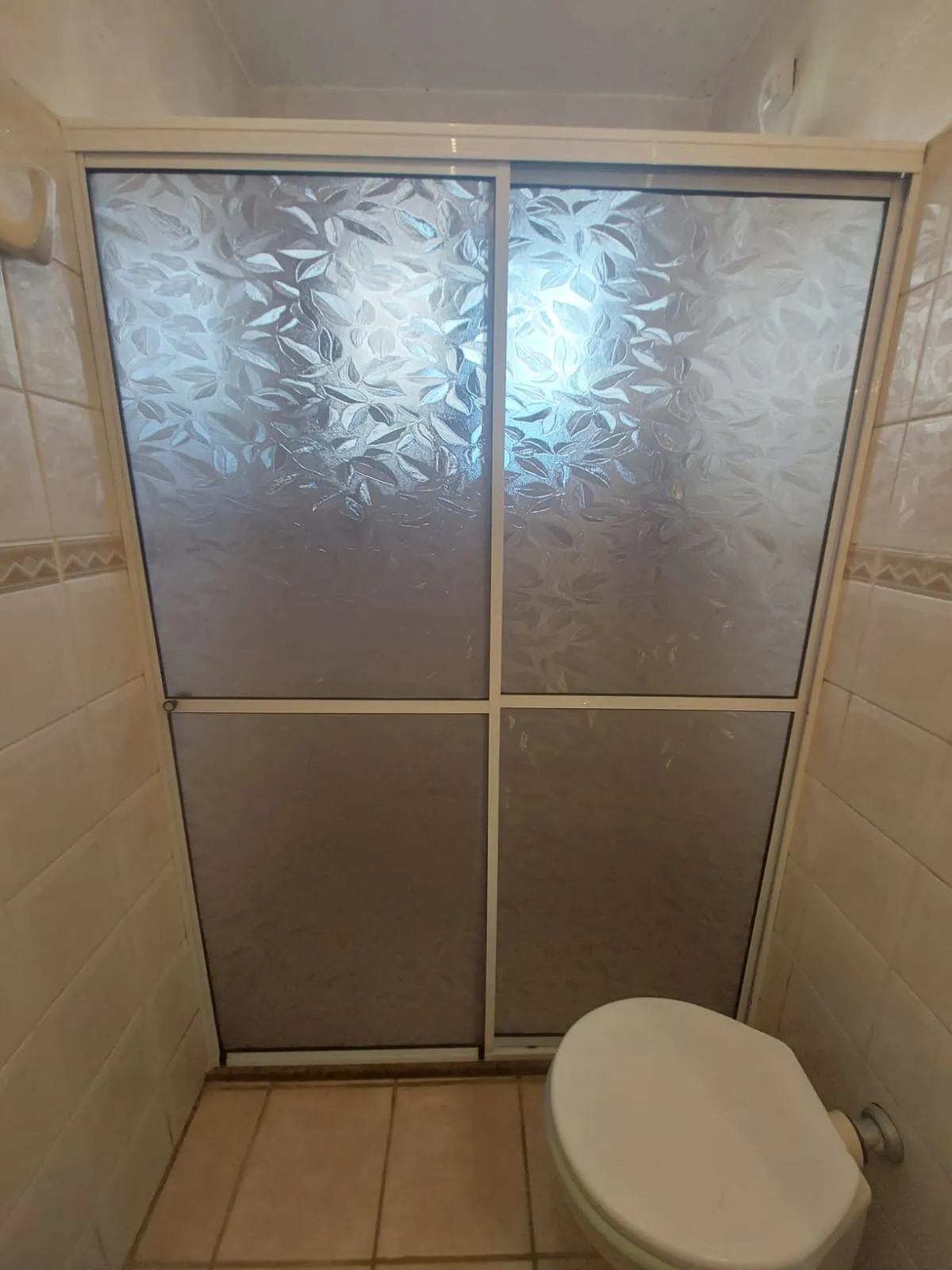 Box de acrílico fumê instalado em banheiro com azulejos brancos